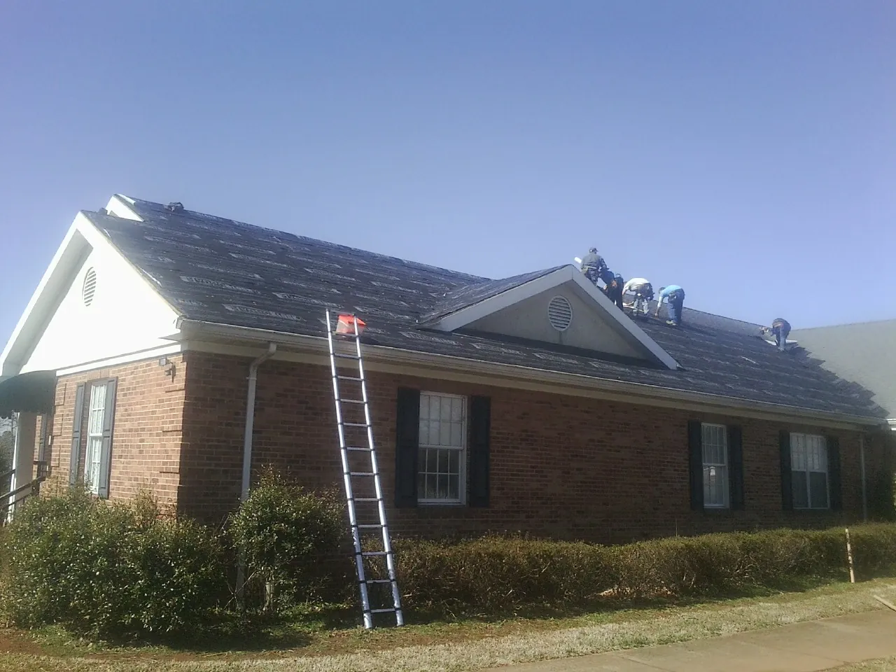 Crew tearing shingles off a brick ranch roof with a ladder set — Emergency Roof Repair work by our crew in Tully