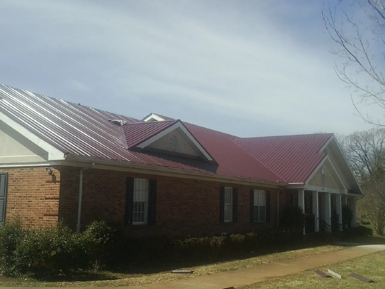 Red metal roof with gabled entries on a long brick building, from a Hail Damage Roof Repair job in Tully