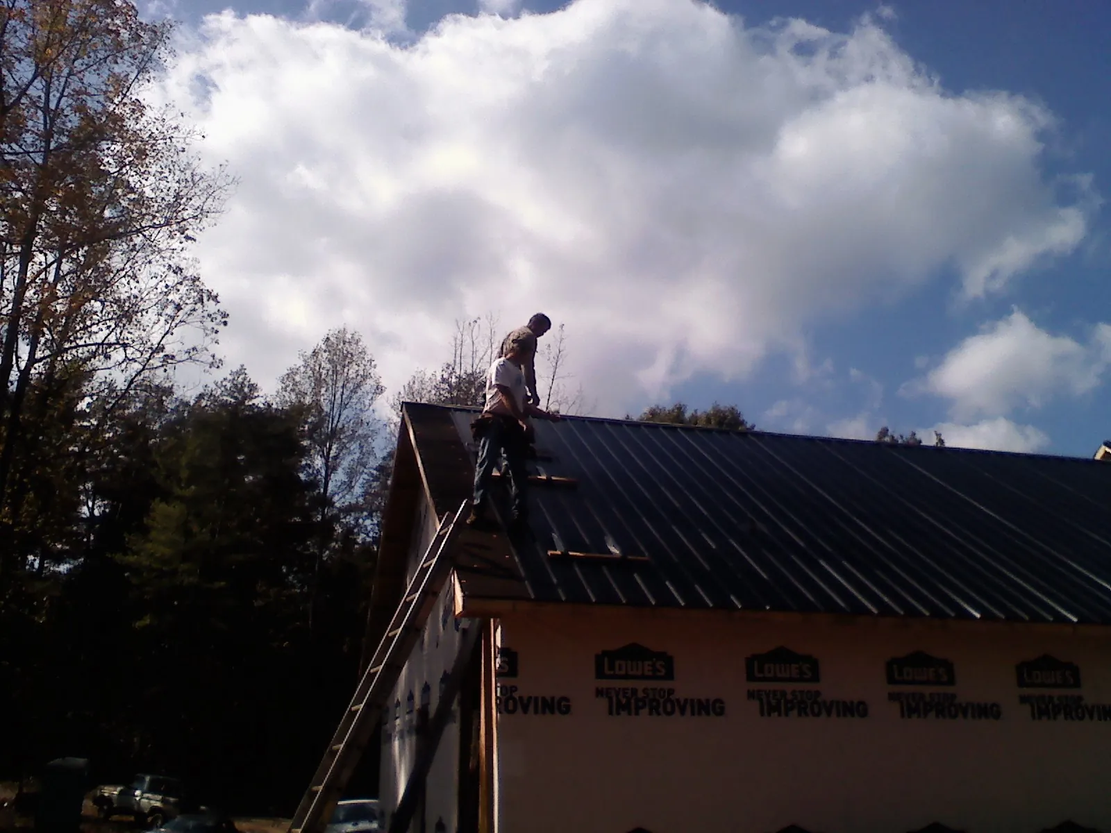 Roofer fastening dark metal panels high against a cloudy sky, from a Roof Inspection job in Tully